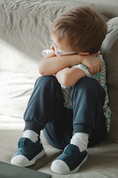 Niño con autismo en gafas se sienta en el sofá y triste