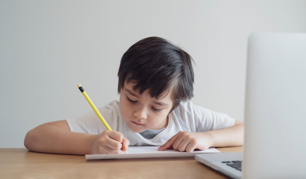 Niño autoaislado usando la computadora para su tarea, Niño usando la computadora portátil buscando información en Internet mientras la escuela está fuera