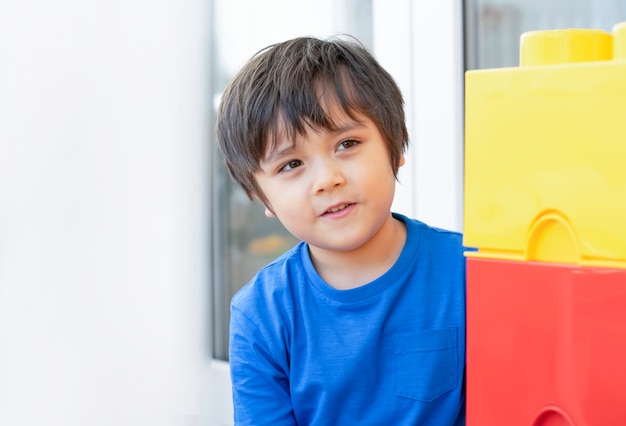 Niño en el autoaislamiento que esconde una caja de plástico colorida, un niño en casa que se divierte jugando a las escondidas en la sala de juegos.