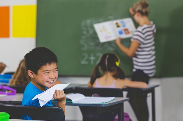 Niño con un avión de papel mientras profesor enseñando en el aula