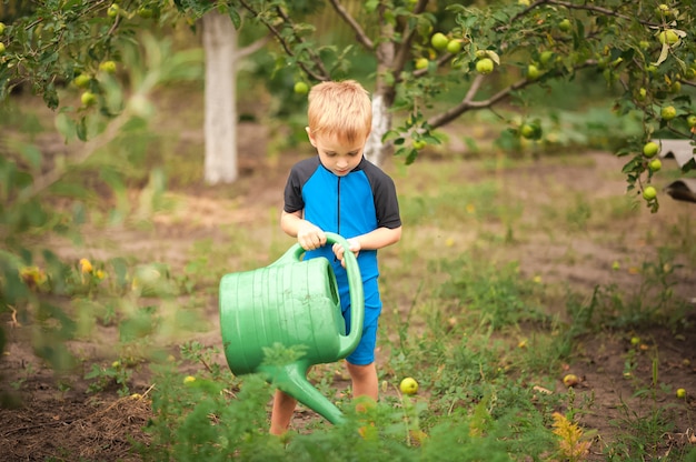 El niño ayuda con el jardín de verano. Juegos infantiles con agua en el patio trasero.