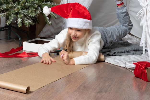 Niño ayudante de Navidad escribiendo una carta a Papá Noel con sombrero rojo niña sonriente haciendo una lista de deseos o una carta a Papá Noel en casa