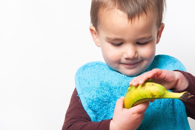 Niño con babero azul tratando de pelar un plátano