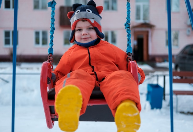 niño se balancea en un columpio en un día de invierno en el patio de recreo