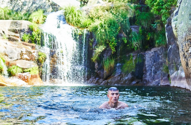 Foto niño se baña en una piscina natural con cascada.