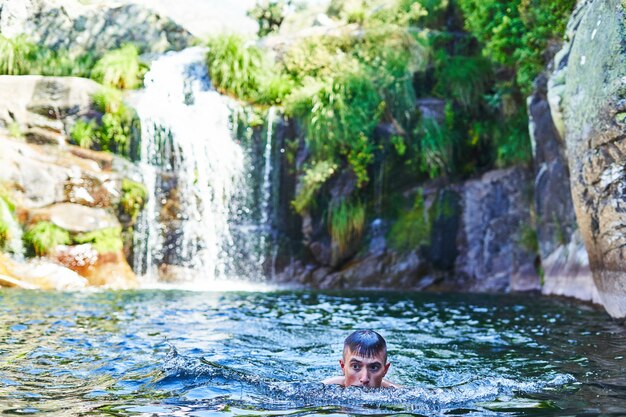 Foto niño se baña en una piscina natural con cascada.