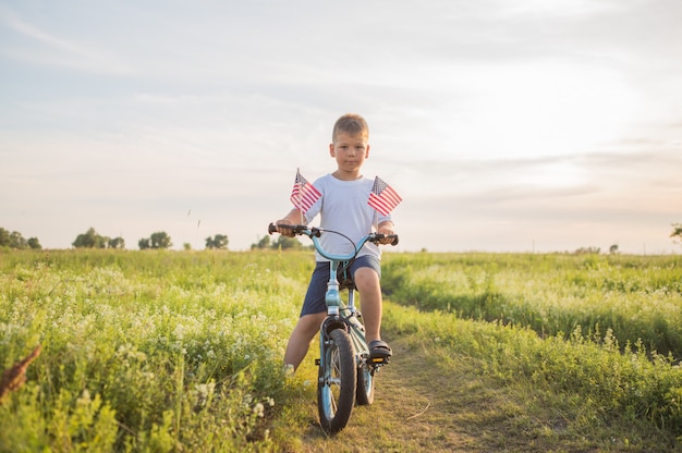 Niño con bandera americana en su bicicleta en el campo verde