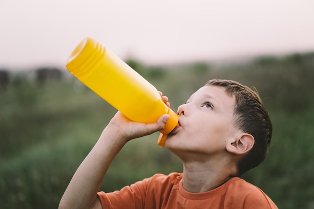 Un niño bebe agua de una botella de naranja mientras camina salud del bebé
