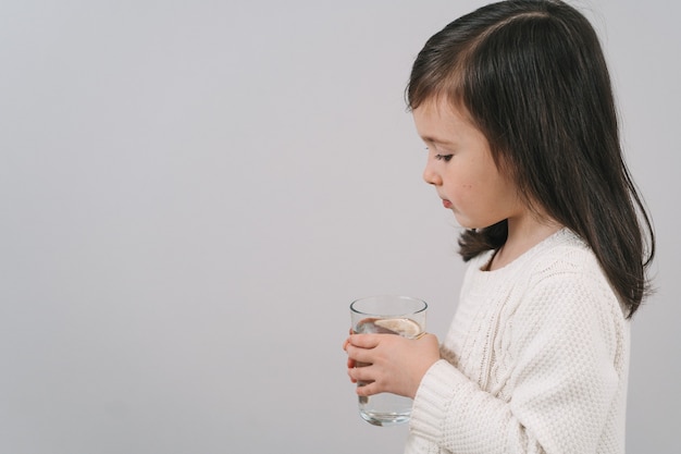 El niño bebe agua de un vaso. Una niña de cabello oscuro sostiene un vaso de agua.