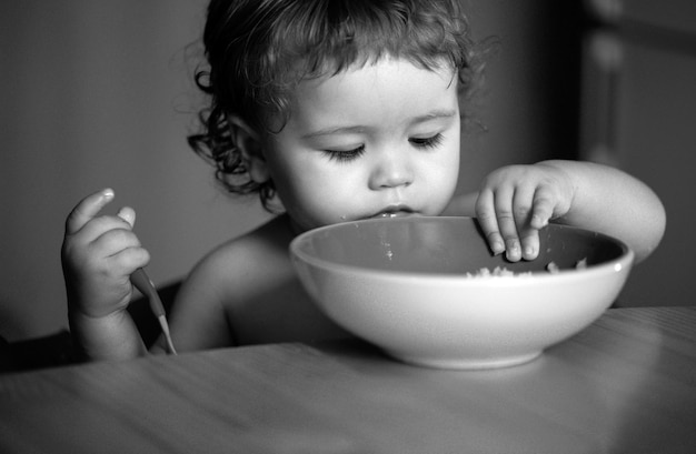 Niño bebé come sopa en la cocina con platos y cuchara