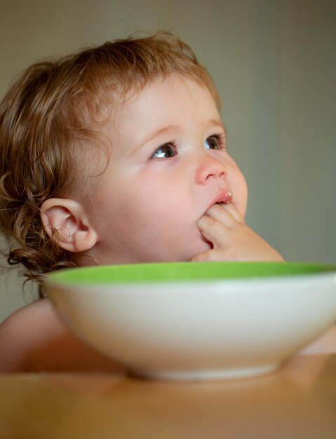 Niño bebé comer sopa en la cocina con platos y cuchara