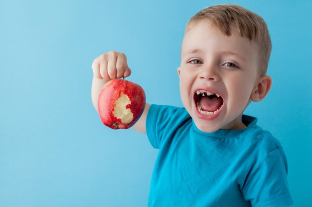 Niño bebé sosteniendo y comiendo manzana roja en azul, comida, dieta y alimentación saludable