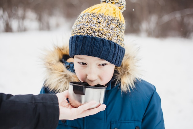 Un niño bebe de un termo de té o una bebida, caminatas de invierno, caminatas, invierno, ropa de invierno