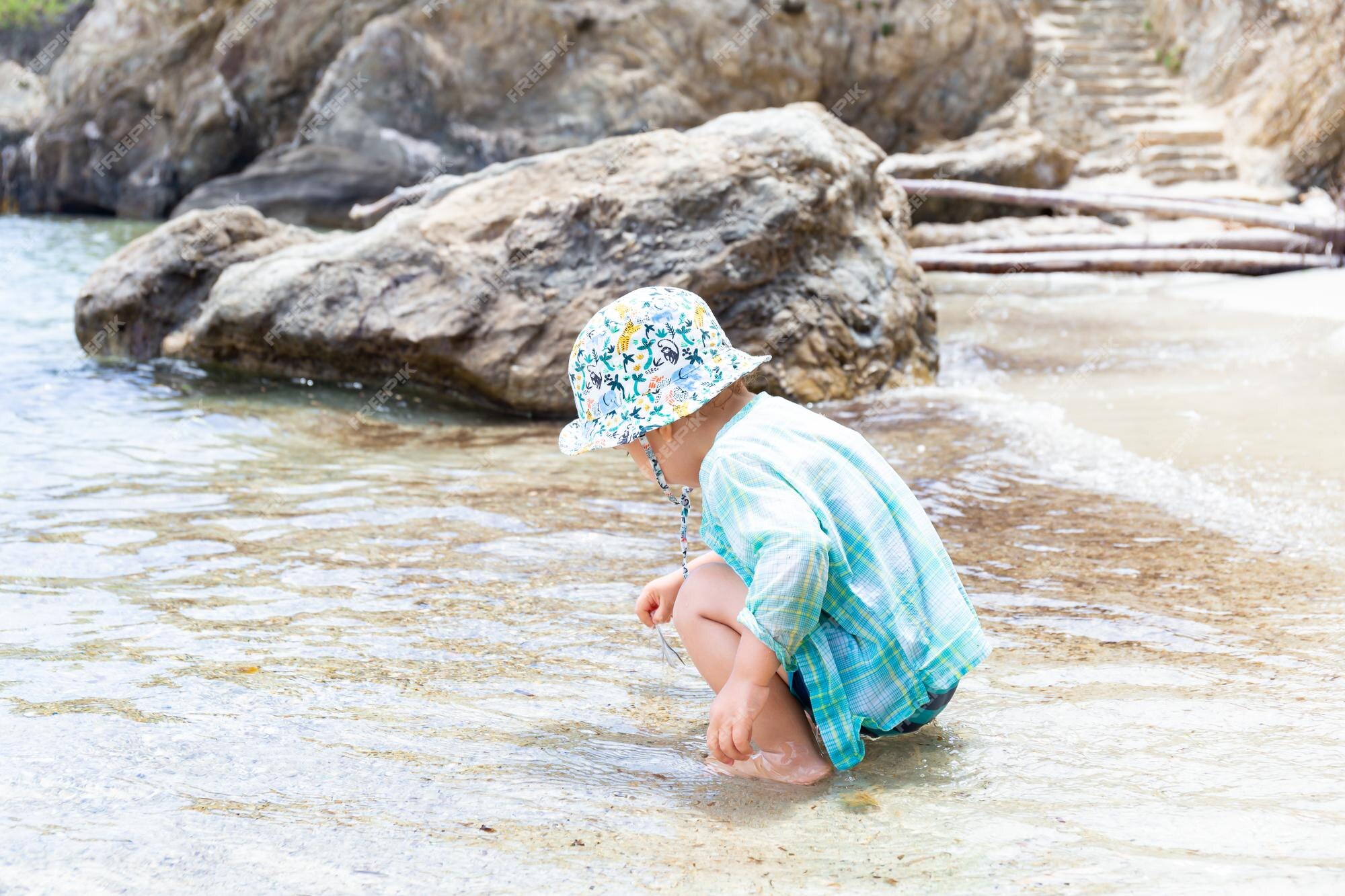 Niño vistiendo ropa de protección solar y panamá está jugando en una costa durante las vacaciones de verano. vacaciones con concepto de niños, espacio de | Foto Premium