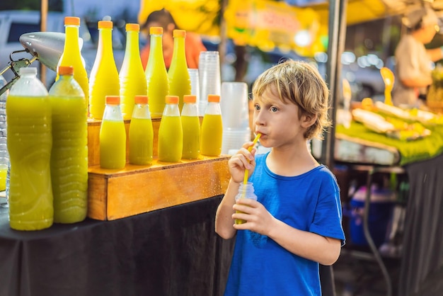 Niño bebiendo jugo de caña de azúcar en el mercado asiático