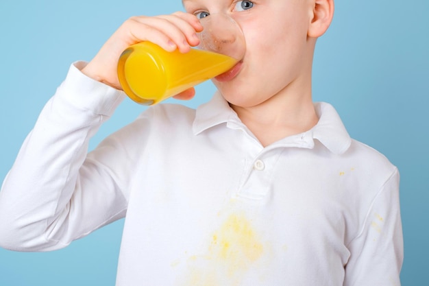 El niño bebiendo jugo recién exprimido mancha sucia de jugo de naranja en la ropa