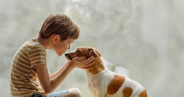 Niño besa al perro en nariz en la ventana.