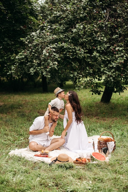 Niño besando a su madre sentada sobre los hombros del padre. Picnic de verano encantador.