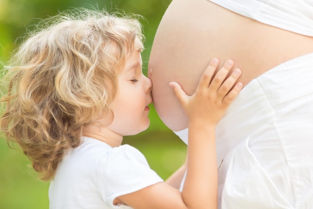 Niño besando el vientre de la mujer embarazada contra el fondo verde primavera