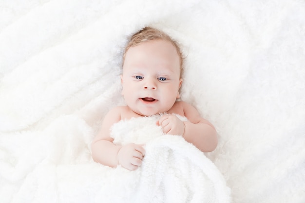 Foto un niño blanco de cuatro meses con ojos azules yace sobre una manta blanca y se cubre con él