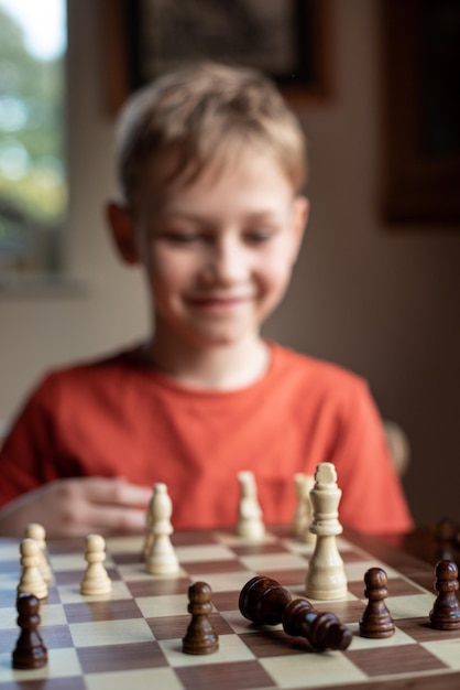 Niño blanco joven jugando un juego de ajedrez en un gran tablero de ajedrez Tablero de ajedrez en la mesa frente al niño de la escuela pensando en el próximo movimiento