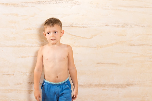 Foto niño blanco en pantalones cortos azules, aislado en la pared de madera marrón.