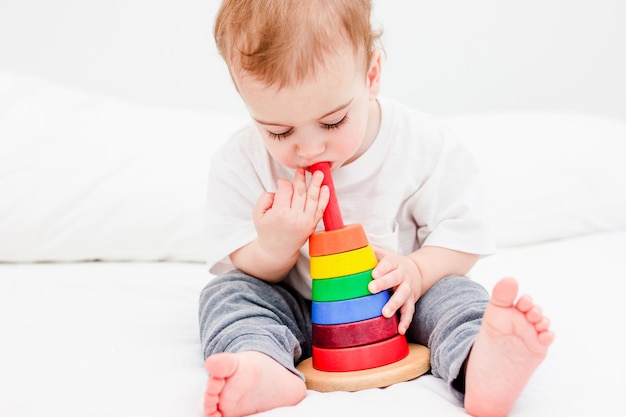 Niño bonito de 1 año con camiseta blanca jugando con pirámide de madera sobre fondo blanco. Concepto de juguete de madera, desarrollo infantil.