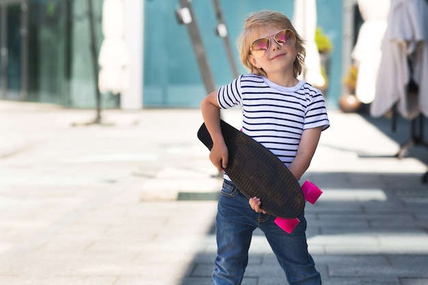 Niño bonito en una tabla de skate. Niño emocional al aire libre. Niño lindo patinaje con gafas de sol.