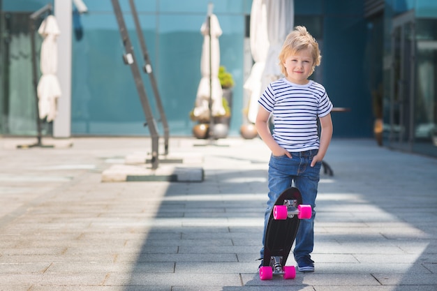 Niño bonito en una tabla de skate. Niño emocional al aire libre. Niño lindo patinaje con gafas de sol.