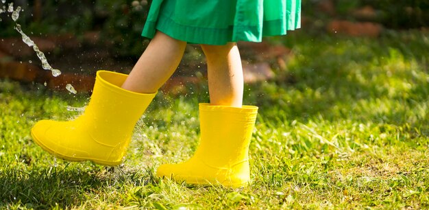 Un niño con botas de goma amarillas brillantes corre por los charcos