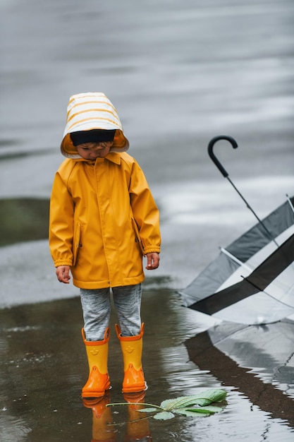 Amperio Excursión Peticionario Niño con botas impermeables amarillas y paraguas jugando al aire libre  después de la lluvia | Foto Premium