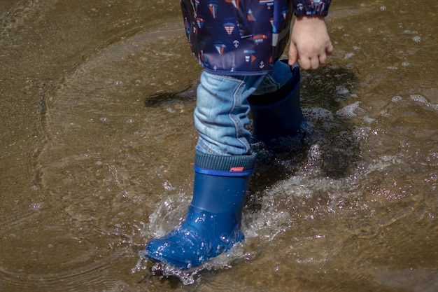 Un niño con botas de lluvia azules chapoteando en un charco