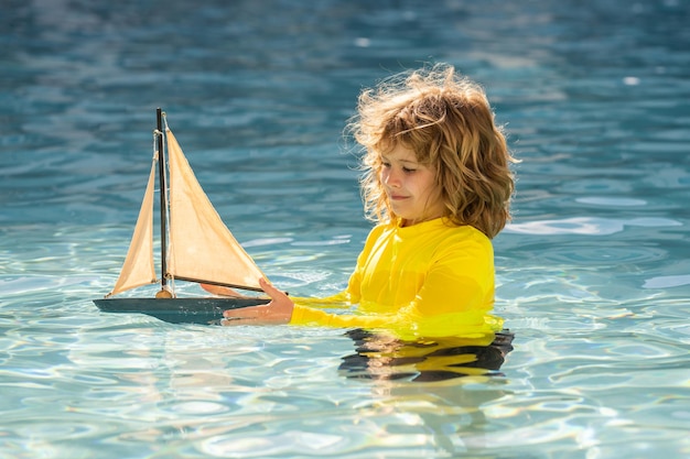 Niño con bote de juguete en agua de mar en vacaciones de verano niño pequeño jugando con bote de juguete en el mar s