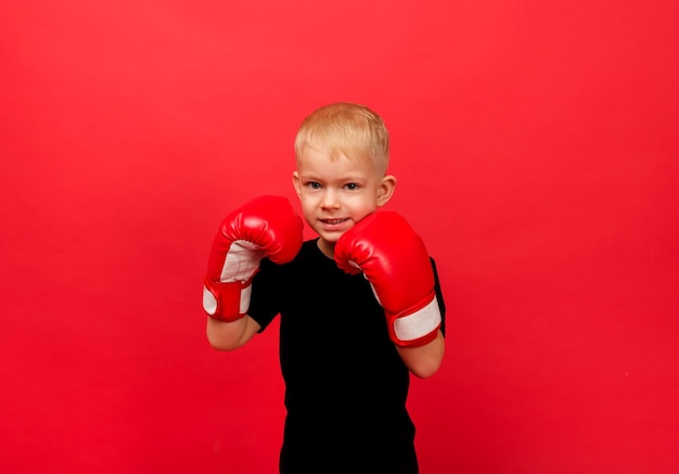 Un niño boxeador en guantes de boxeo rojos se encuentra en un stand en rojo