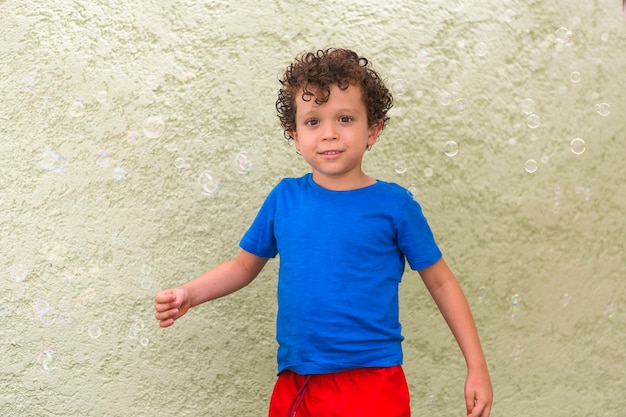 Niño con cabello rizado y apariencia caucásica mirando a la cámara rodeado de pompas de jabón