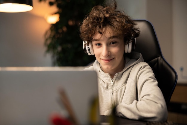 Un niño con cabello rizado está feliz con el aprendizaje remoto Un estudiante se sienta frente a una computadora con auriculares inalámbricos escuchando una conferencia del maestro Las lecciones se llevan a cabo a través de Internet