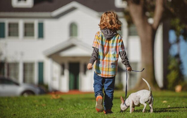 Niño y cachorro fuera de niño feliz niño y perro jugando en el césped del patio trasero mascota caminando