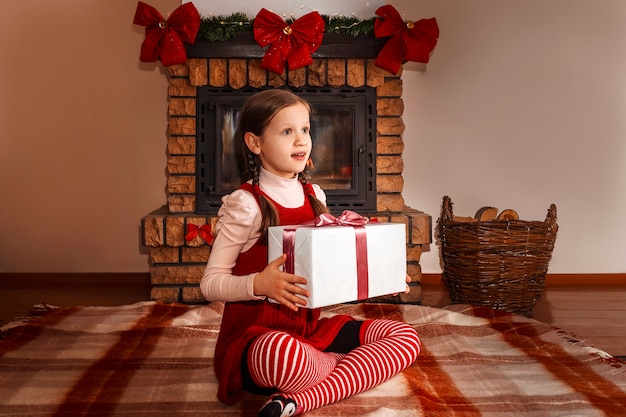 Niño con una caja de regalo en el fondo de una chimenea de Navidad decorada