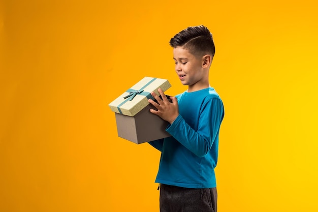 Foto niño con una caja de regalos y mirando dentro de la caja sobre un fondo amarillo concepto de cumpleaños y celebración