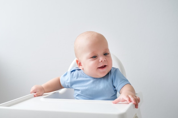 niño calvo de 3 meses sentado en una silla de bebé sobre fondo blanco