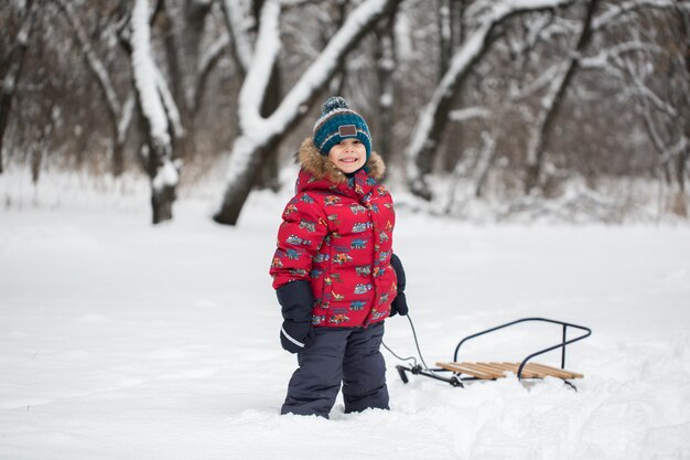 Niño caminando con trineos en bosque de invierno cubierto de nieve