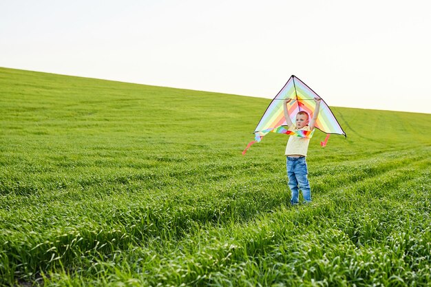 Niño con camisa amarilla corriendo con cometa en el campo el día de verano