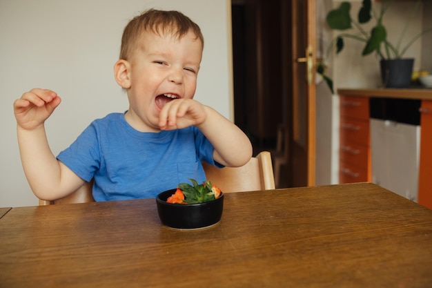 Un niño con una camisa azul se sienta en una mesa con un plato de sushi.