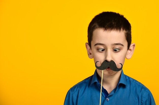 Foto un niño con una camisa azul sobre fondo amarillo está retorcido y viste su bigote