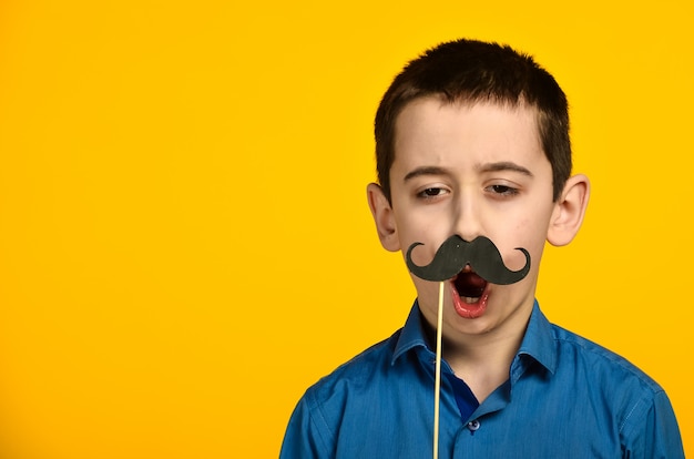 Foto un niño con una camisa azul sobre fondo amarillo está retorcido y viste su bigote