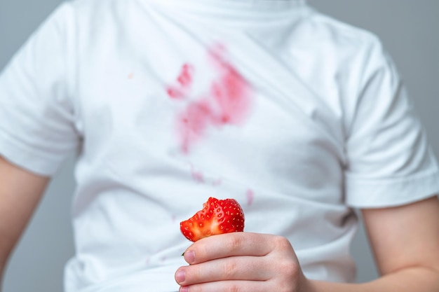 Un niño con una camisa blanca con una fresa.