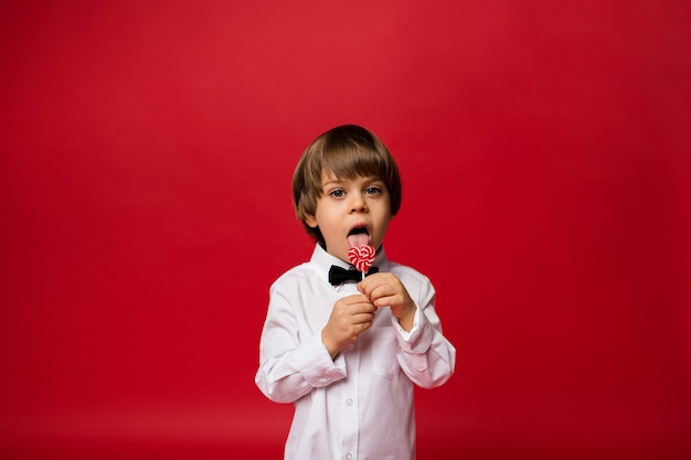 Foto un niño con una camisa blanca lame una piruleta en rojo
