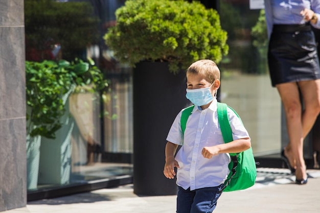 Un niño de camisa blanca con una máscara protectora y una mochila a la espalda se apresura a ir a la escuela el primer día de clases después del aislamiento o las vacaciones Nuevas reglas de seguridad en la escuela