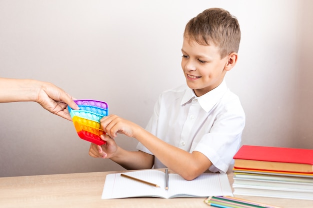 Un niño con una camisa blanca se sienta en una mesa y toma una burbuja eterna de las manos de una mujer para jugar con un juguete, no para estudiar.