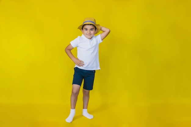 un niño con una camisa blanca y un sombrero de paja en una pared amarilla.